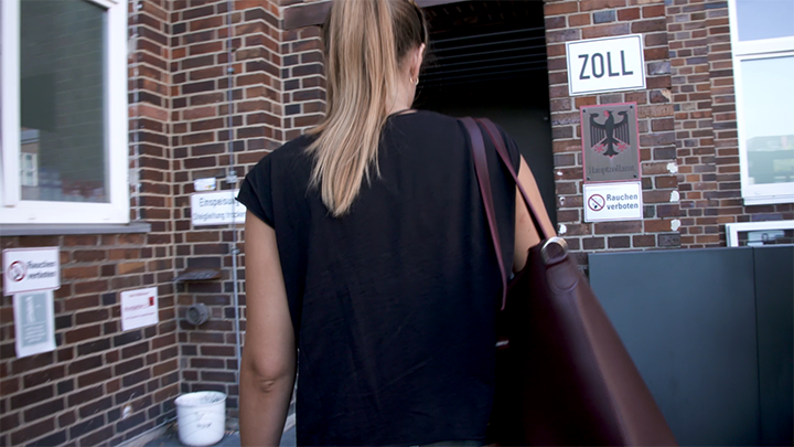 Eine junge Frau mit Tasche um Ihre Schulter betritt ein Gebäude des Zolls.